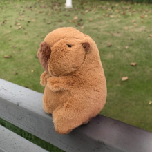 Load image into Gallery viewer, Capybara Plushie Sitting on a Railing with a Grassy background - Tinyminymo