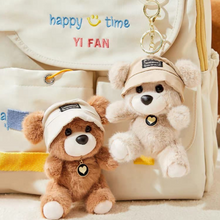 Load image into Gallery viewer, Cute Teddy Plush Keychain with hat in front of a beige bag with 'happy time YI FAN' text - Tinyminymo