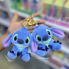 Load image into Gallery viewer, Two Blue Plush Stitch 3D Keychains Held in Hand Against a Blurred Store Background - Tinyminymo