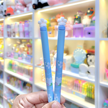 Load image into Gallery viewer, Two Blue Sakura Gel Pen ends held in front of a colorful store display - Tinyminymo