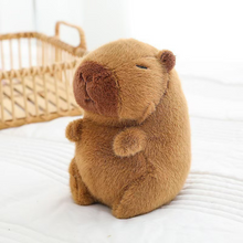 Load image into Gallery viewer, Capybara Plushie on a White Surface with a Wicker Basket in the Background - Tinyminymo
