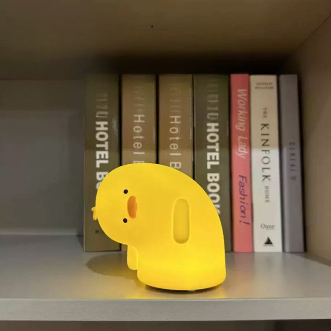 Crooked Neck Duck Silicone Night Light Glowing Yellow, Placed on Wooden Book Rack in Front of Books - Tinyminymo