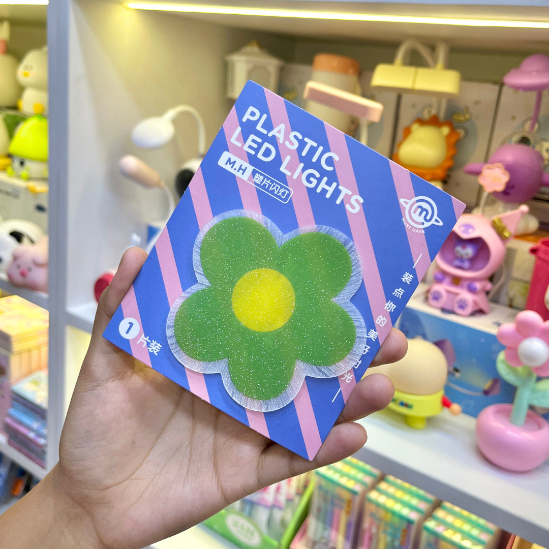 A Hand Holding a Piece of Cute Flower Stick on Light in Green Color displayed in front of a store - Tinyminymo