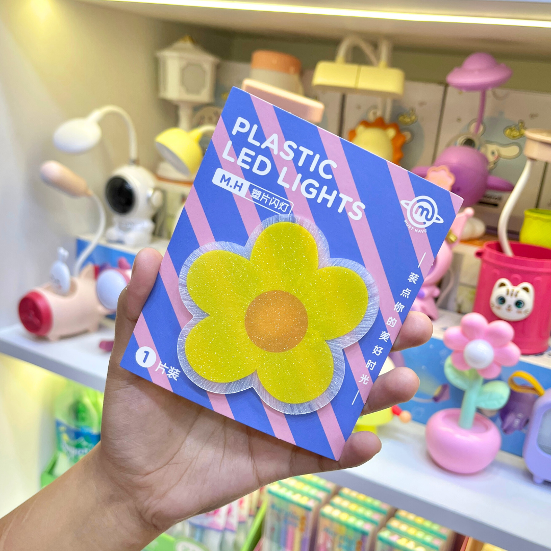 A Hand Holding a Piece of Cute Flower Stick on Light in Yellow Color against a vibrant, colorful background - Tinyminymo