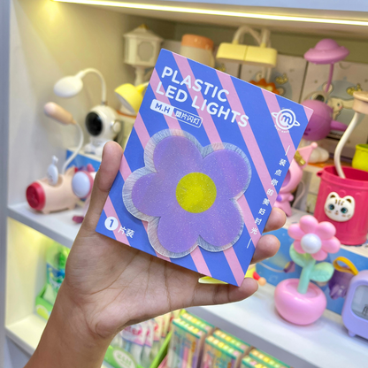 Hand holding a Piece of Cute Flower Stick on Light in Purple Color against a toy store background - Tinyminymo