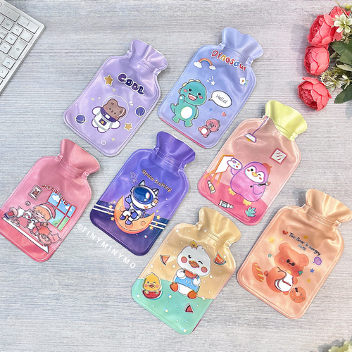 A vibrant set of cartoon-themed Cute Hot Water Bags arranged on a light grey surface, with flowers and a Keyboard in the Background - Tinyminymo
