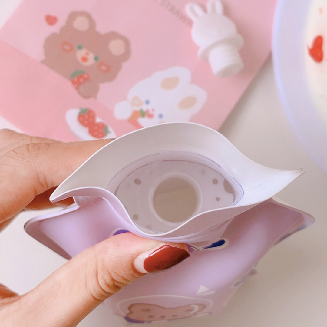 Pink silicone Hot Water Bag with cartoon designs held by a hand - Tinyminymo