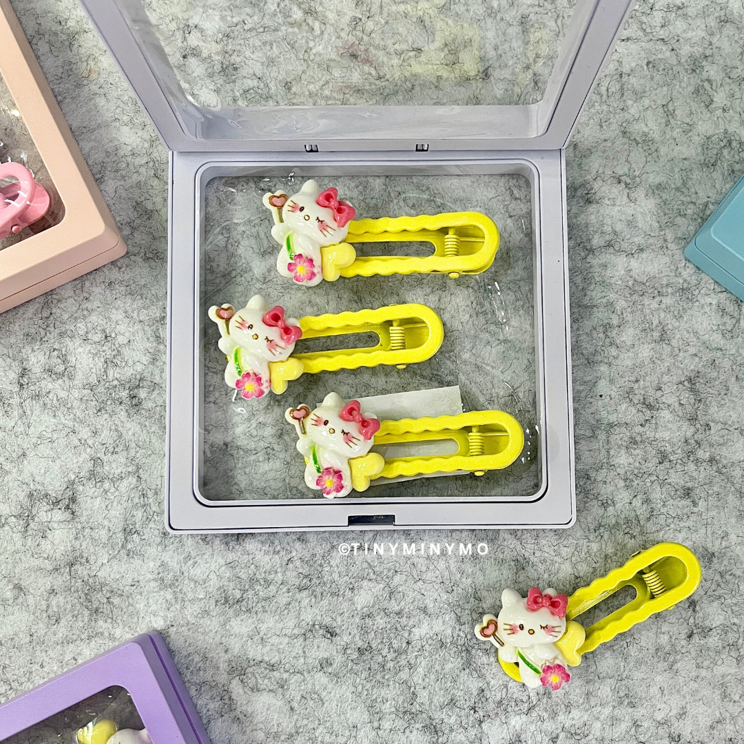 Three Yellow Cute Kitty Hair Clips with Cat Designs in a Clear Container Placed on a Grey Surface - Tinyminymo