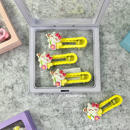 Three Yellow Cute Kitty Hair Clips with Cat Designs in a Clear Container Placed on a Grey Surface - Tinyminymo