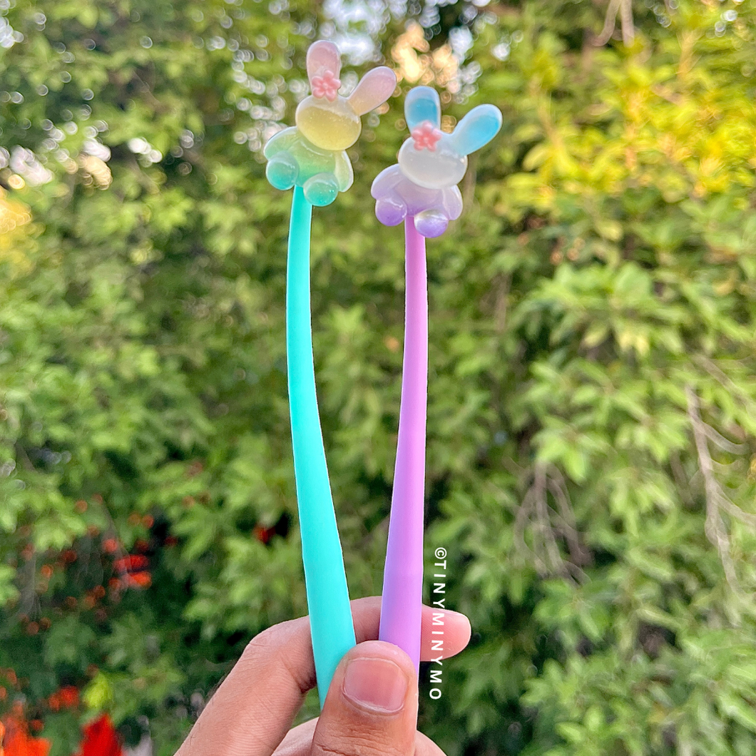 Two Colorful Dancing Bunny Gel Pens with Cute Bunny Designs Held Against a Green Outdoor Background – Tinyminymo