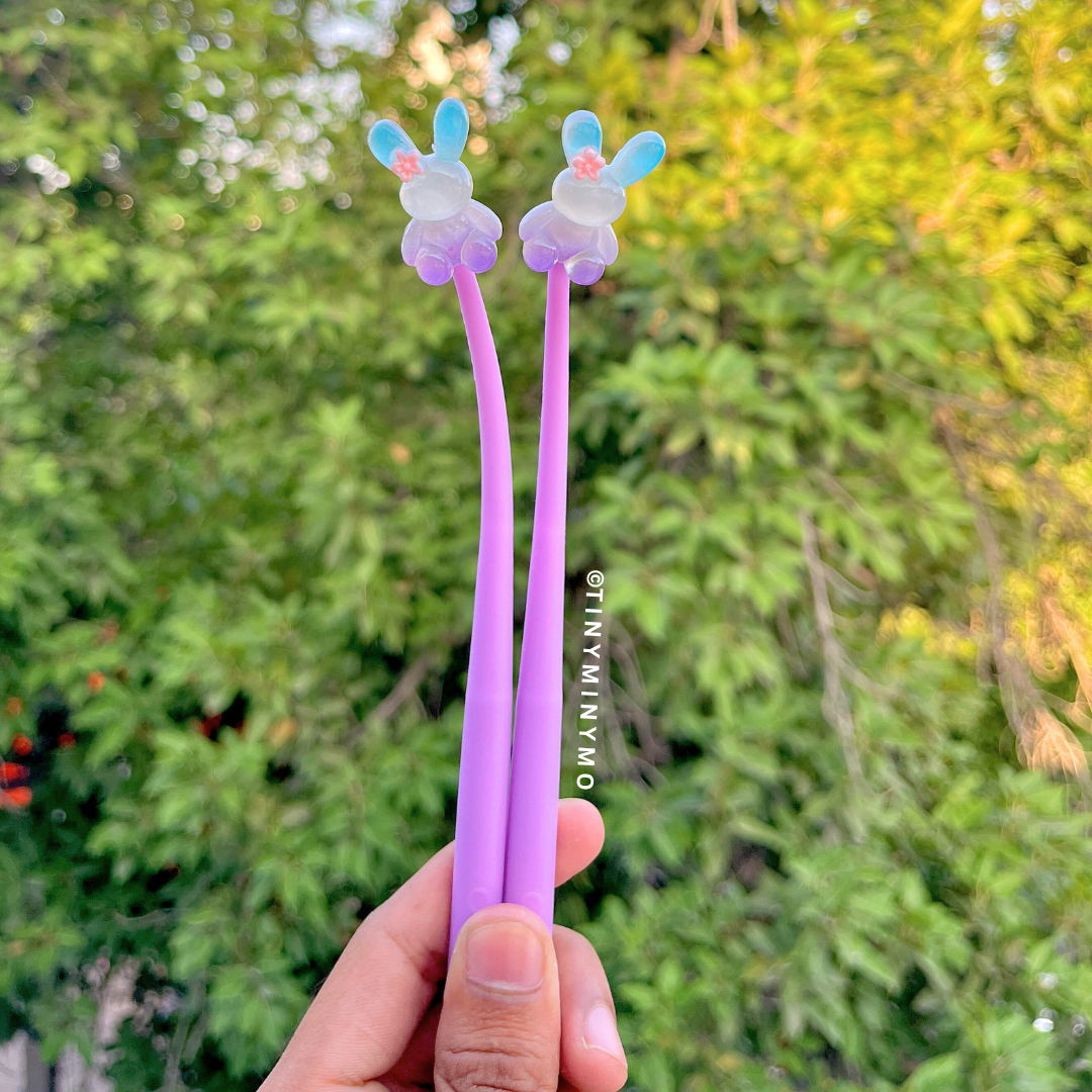 Two Purple Dancing Bunny Gel Pens with Bunny Design Held in Front of a Blurred Green Outdoor Background - Tinyminymo