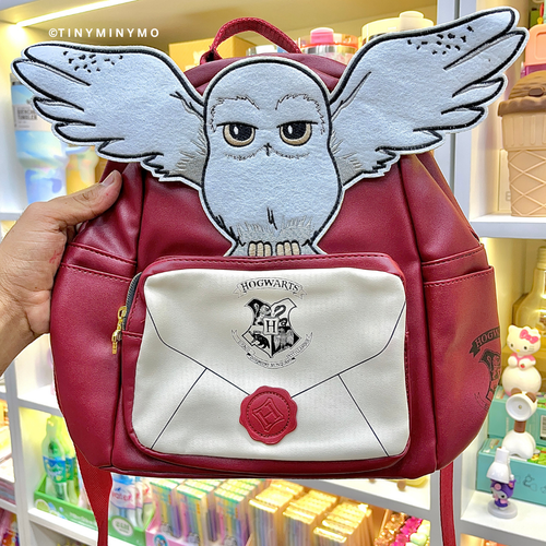 Red Harry Potter's Hedwig Backpack with Owl Design and 'Hogwarts' Emblem Held in Front of a Store Shelf - Tinyminymo