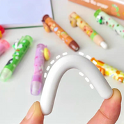 White U-shaped Kawaii Push Eraser Held by a hand with Colorful Kawaii Erasers in the Background - Tinyminymo