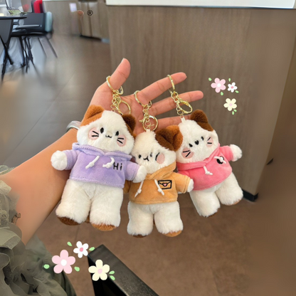 A Lady Holding Three Kitty-in-Hoodie Plush Keychains in Three Different Hoodie Colors, Each Kitty Displaying a Different Expression, Set Against a Cafeteria Background - Tinyminymo