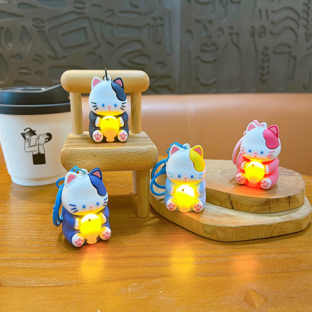 Four Different Colored Lightup Cat Keychain Placed on Wooden Surface or Wooden Chair with Cute Lightning Fish in their Hands - Tinyminymo