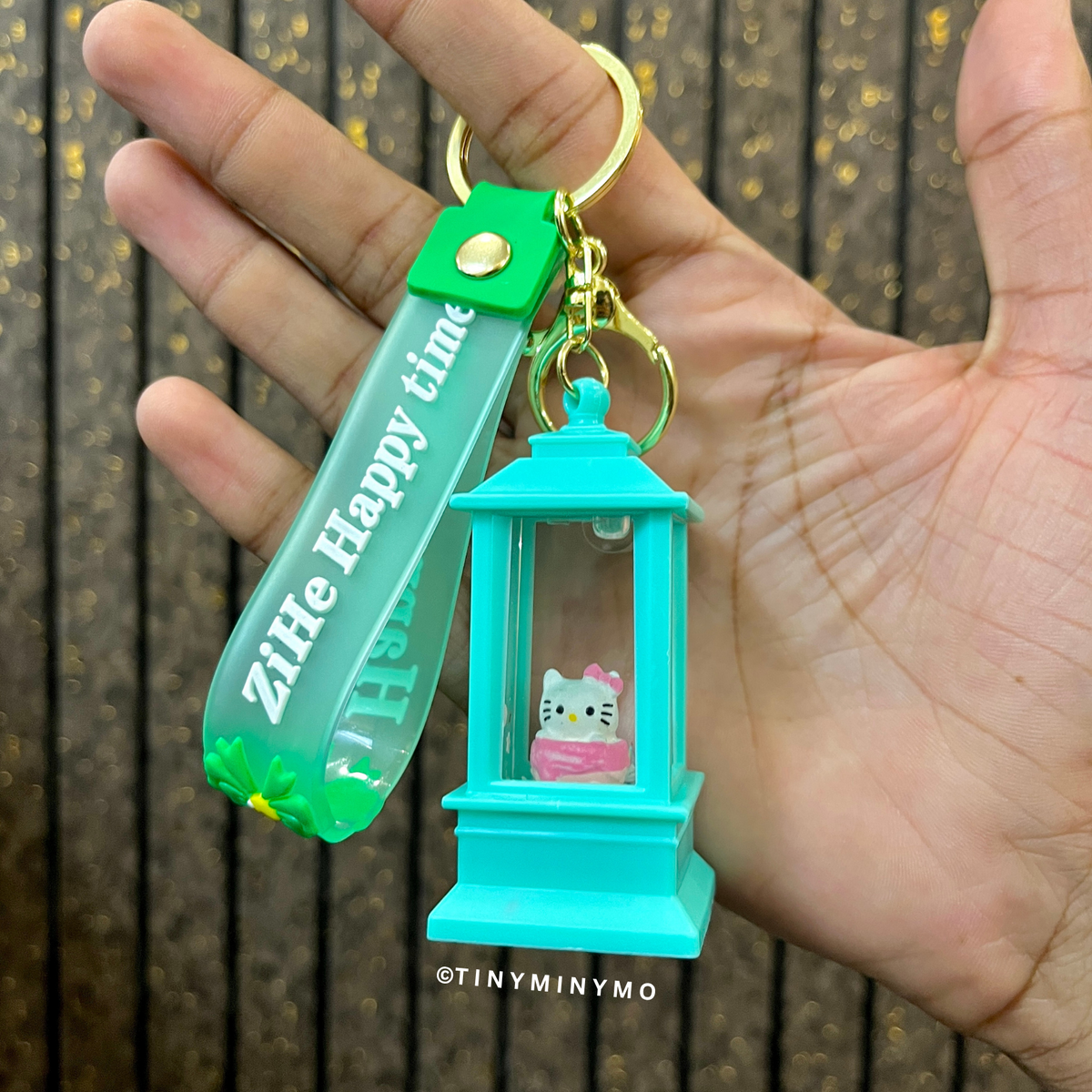 Lightup Sanrio Keychain with a Small Hello Kitty Figure and Green Tag Held in a Hand Against a Wooden Background - Tinyminymo
