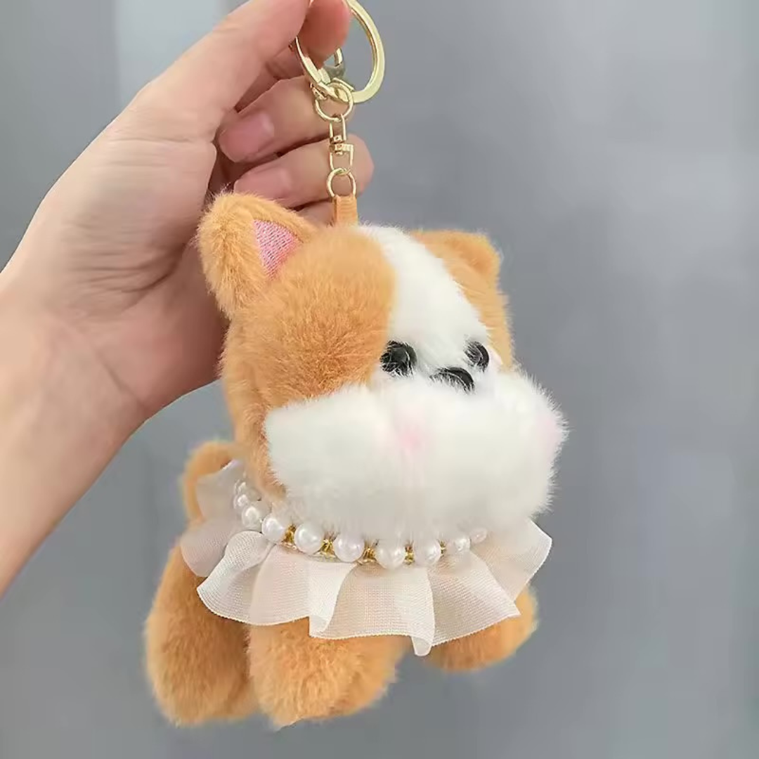 Pretty Puppy Plush Keychain in Beige Color with a Pearl Necklace held by a hand against a grey background - Tinyminymo