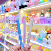 Three Sakura Gel Pen held in front of a store shelf with toys and stationery - Tinyminymo