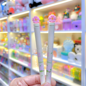 Two White Sakura Gel Pen held in front of a colorful store display - Tinyminymo