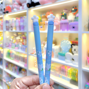 Two Blue Sakura Gel Pen ends held in front of a colorful store display - Tinyminymo