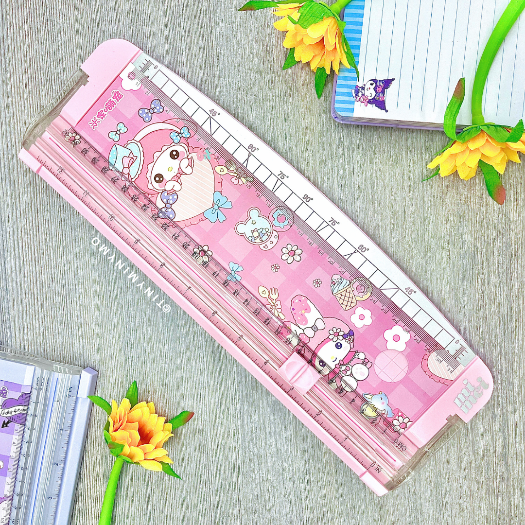 Pink Sanrio Paper Trimmer with My Melody Print, Displayed on a Wooden Surface with Flowers and Stationery Items - Tinyminymo